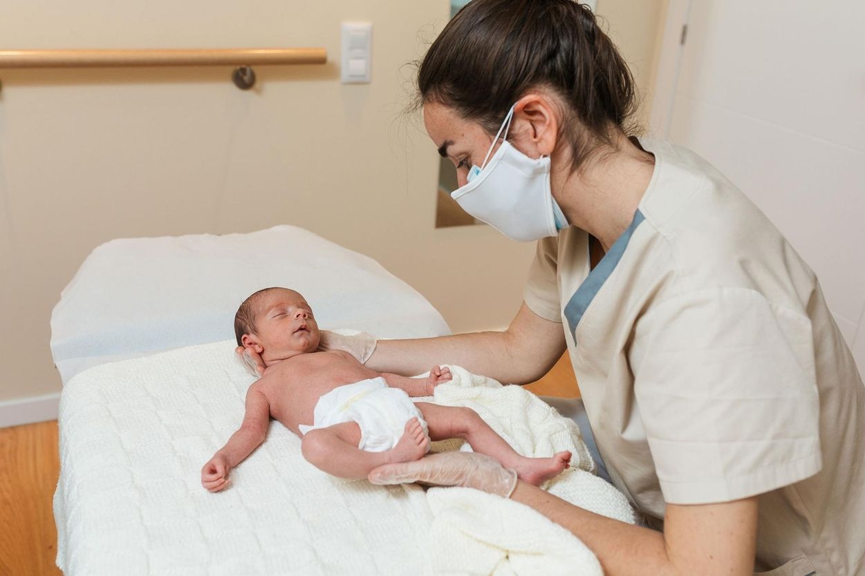 Therapeutin behandelt Neugeborenes mit sanfter Berührung auf Behandlungsliege - Anwendung craniosacraler oder osteopathischer Therapie bei Babys