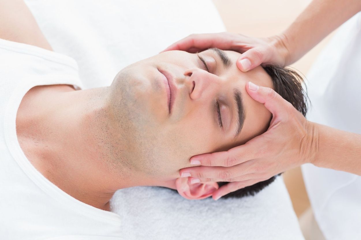 Mann liegt entspannt auf Behandlungsliege und erhält sanfte manuelle Therapie am Kopf - Symbolbild für Stressabbau Entspannung und ganzheitliche Behandlung im Therapiezentrum