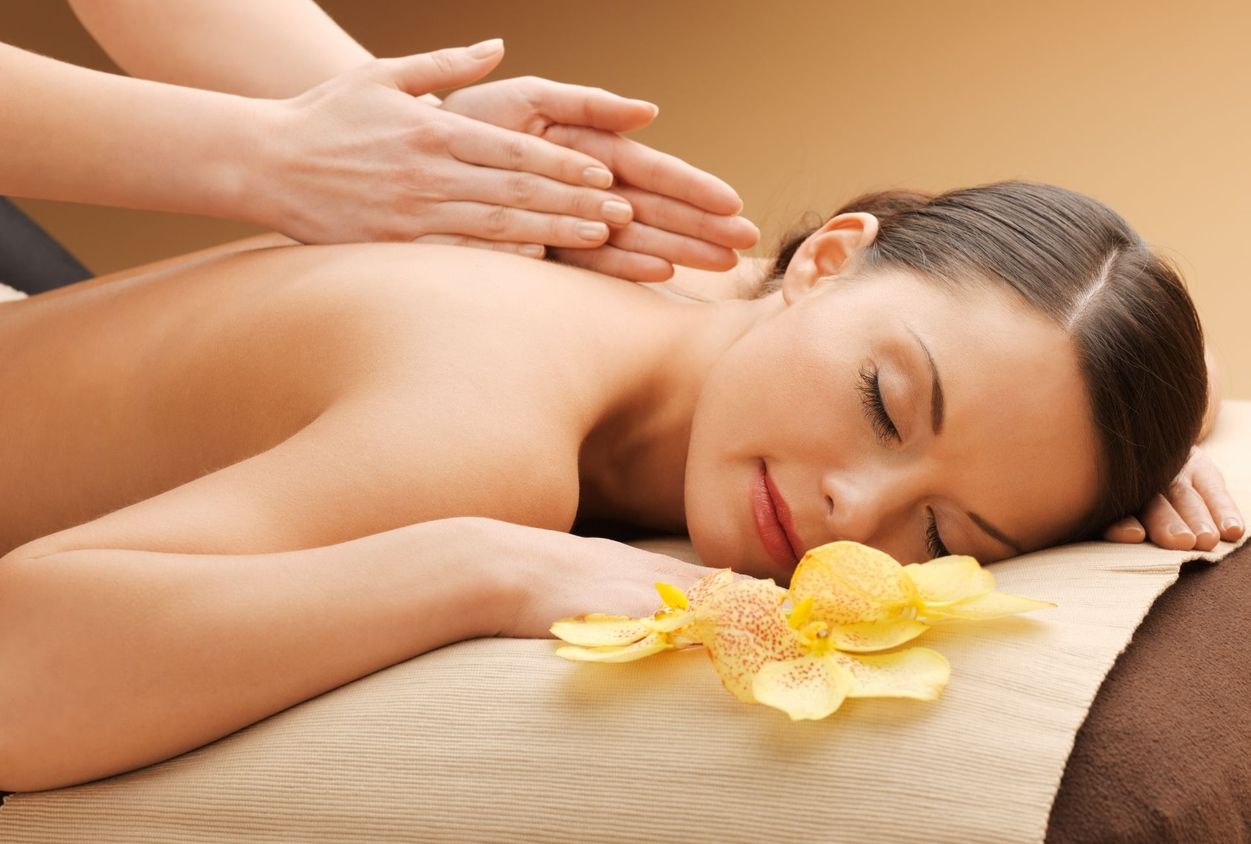 Frau entspannt bei Rückenmassage mit geschlossenen Augen und Blüte auf der Liege